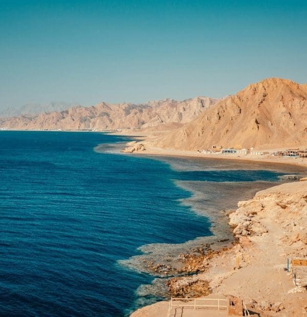 Rocky coastline with blue sea and mountains.