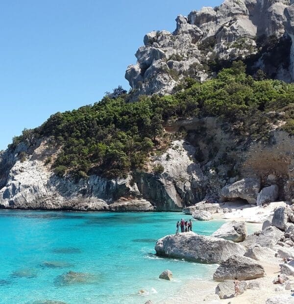 Turquoise sea with rocky cliffs and beachgoers.