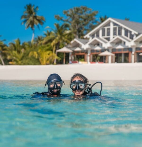 Two scuba divers in tropical water near beachfront villa.