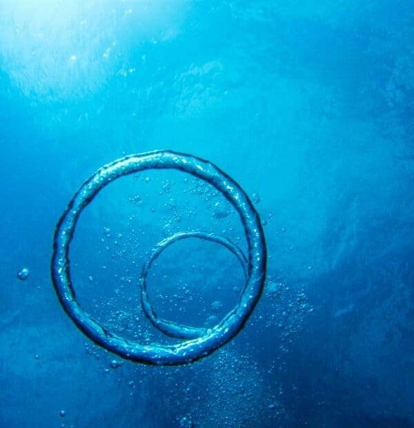 Underwater air bubble ring ascending in blue ocean waters.