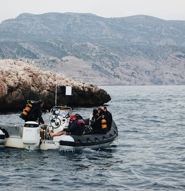 Divers preparing on boat near rocky coastline.