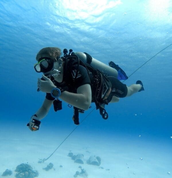 Scuba diver exploring underwater with camera in clear ocean.