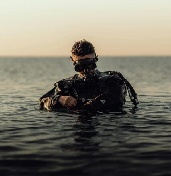 Scuba diver adjusting gear in tranquil sea at sunset.