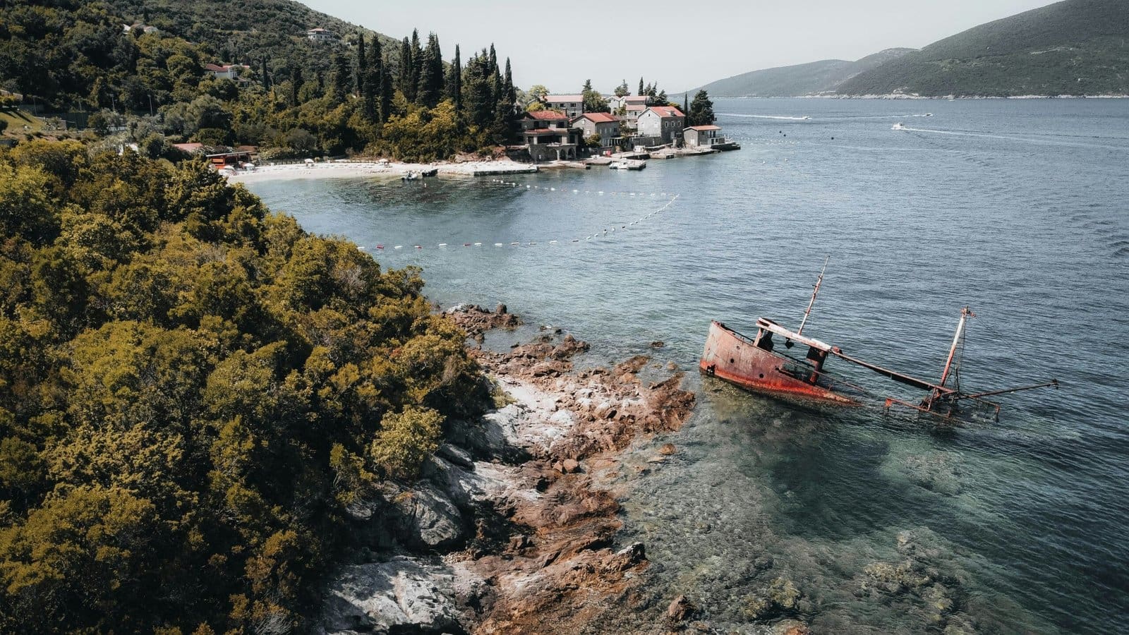 Sunken ship near coastal village with lush greenery