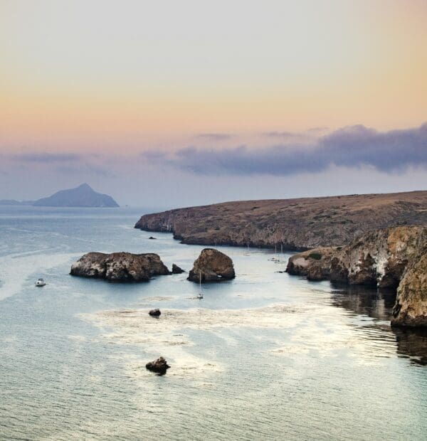 Coastal sunset over serene bay with cliffs and boats.