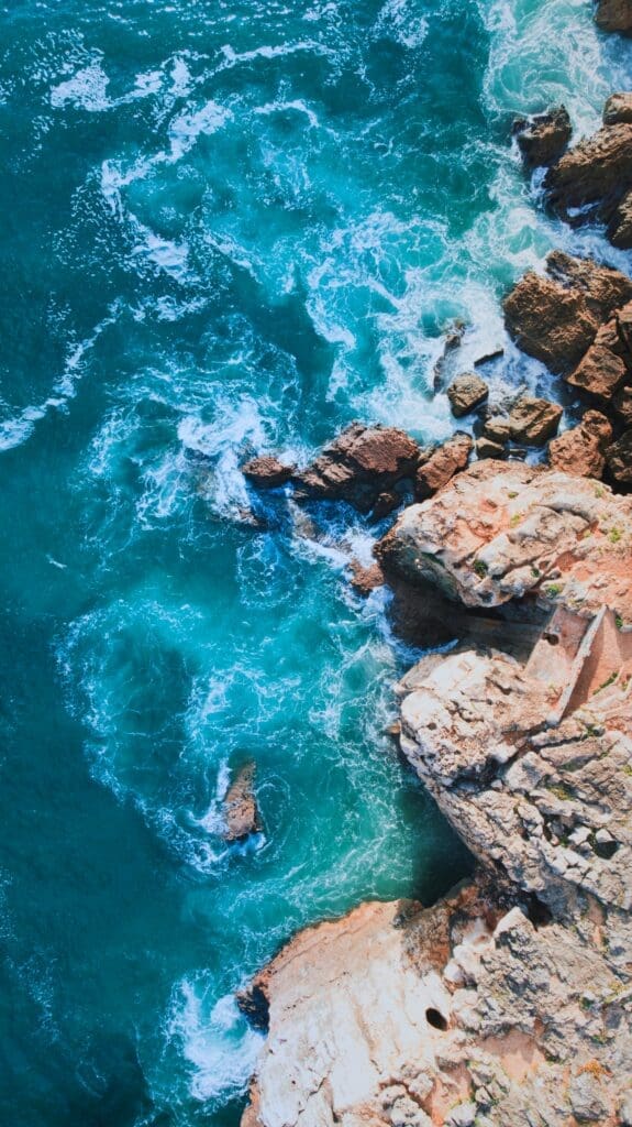 Aerial view of turquoise sea waves crashing on rocky coast