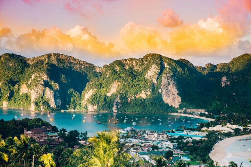 Tropical beach with boats and lush cliffs at sunset